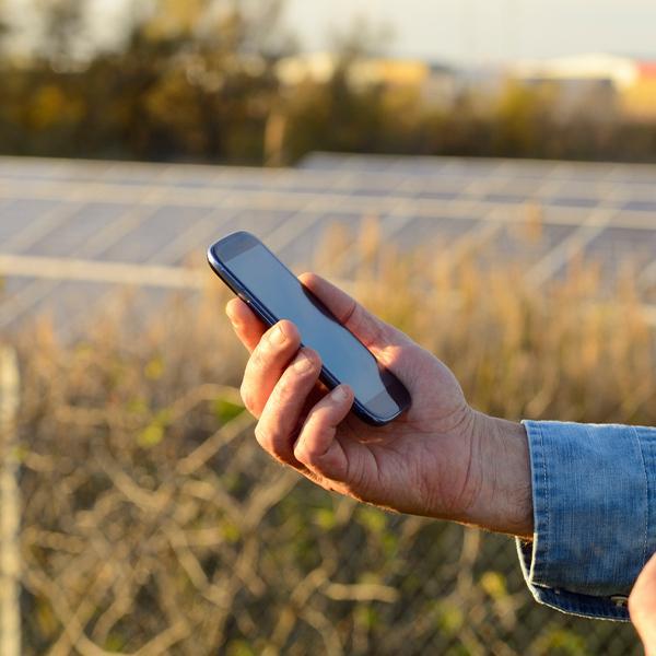 Smartfon w dłoni na tle paneli słonecznych